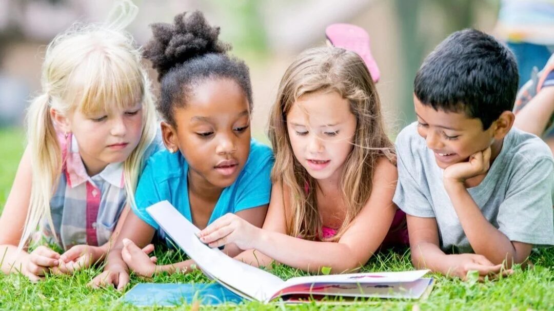 Four children lying on the grass, reading a picture book together