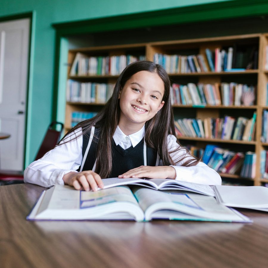 A smiling student reading an open book in a library