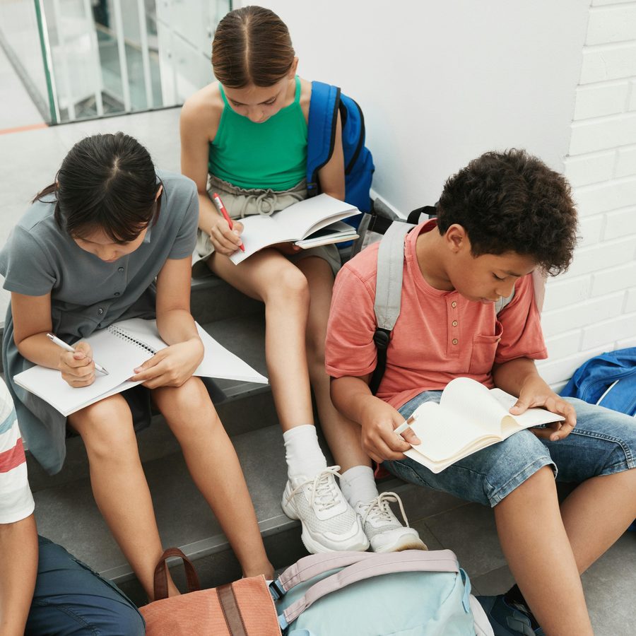 Three students sitting together reading and writing in notebooks